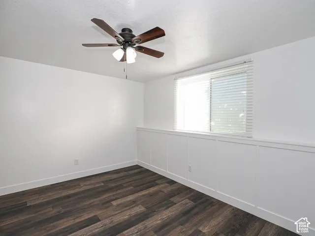 Room featuring wood-finish flooring, white board-and-batten wainscoting, a ceiling fan with integrated lighting, and a sliding window with horizontal blinds