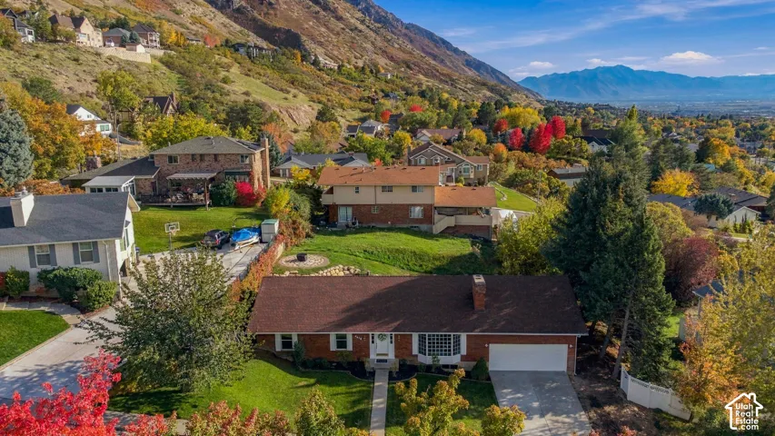 Aerial perspective featuring a brick exterior residence with a multi-gabled roof, an attached garage, a concrete driveway, and established landscape