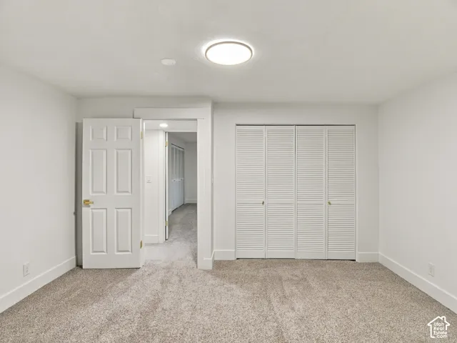 Neutral interior room featuring neutral carpeting, a flush-mount overhead light fixture, a six-panel interior door, and a four-panel louvered bi-fold closet door