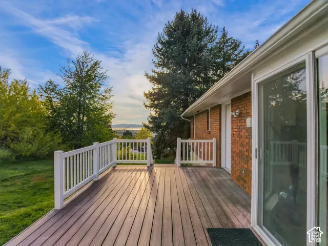 Raised exterior deck with composite decking, white balustrade railing, brick siding, and full-height sliding glass doors