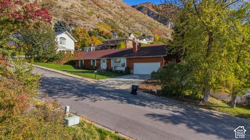 Brick exterior residence featuring a composition shingle roof, attached garage, concrete driveway, and mountain backdrop