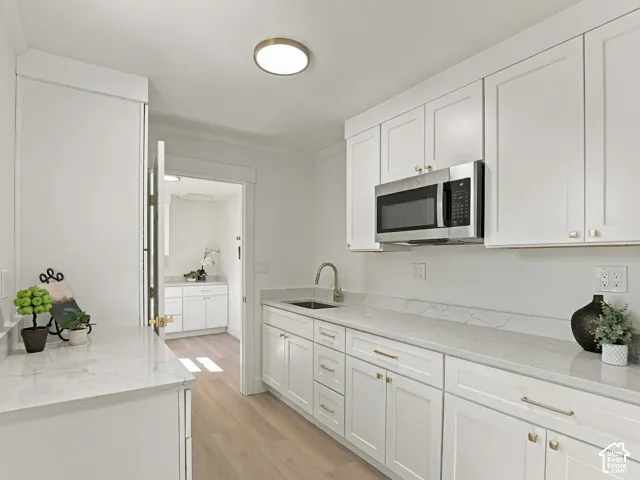 Kitchen featuring white shaker-style cabinetry, quartz countertops with matching backsplash, stainless steel built-in microwave, under-mount sink with pull-down faucet, and wood-finish flooring