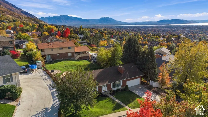 Aerial perspective featuring a brick exterior residence with a composition shingle roof, a two-car garage, an established lawn, and a mountain and valley backdrop