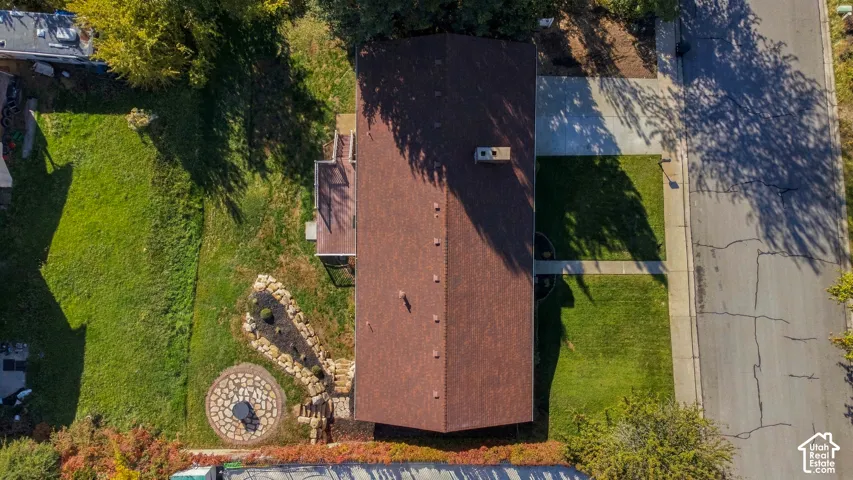 Aerial view of the property featuring a structured hardscape patio, stone-bordered landscaping, a concrete walkway, and an asphalt roof