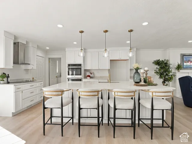 Kitchen featuring a center island with a stone countertop, white cabinetry, integrated stainless steel appliances, and three metallic pendant lights, complemented by wood-finish flooring