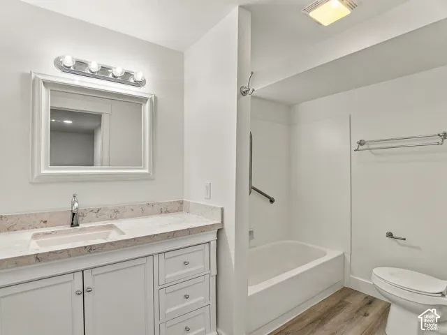 Bathroom featuring a white vanity with drawers and cabinets, a patterned countertop with an integrated sink, a rectangular mirror with a white frame, a bathtub and shower combination, and wood-finish flooring