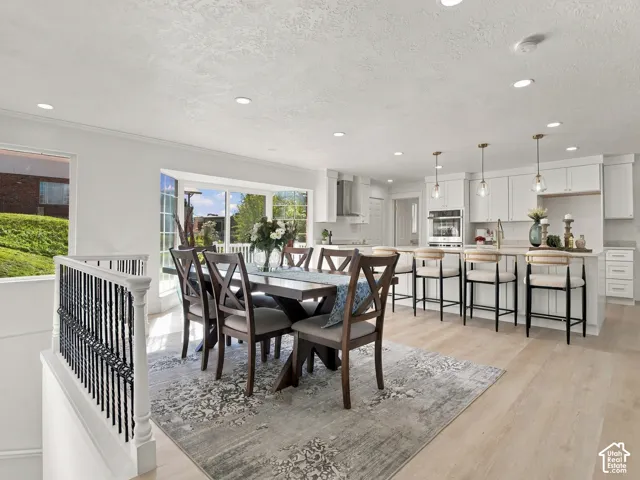 Open-concept kitchen and dining area featuring white shaker-style cabinetry, a central island with bar seating, wood-finish flooring, recessed lighting, and a large sliding glass door
