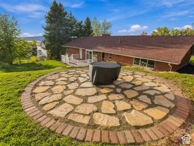 Circular flagstone patio with a brick border, elevated wood deck with white railings, and brick exterior finish
