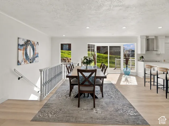 Open-concept area featuring light-toned wood-finish flooring, recessed lighting, sliding glass patio doors, and a metal-balustrade staircase