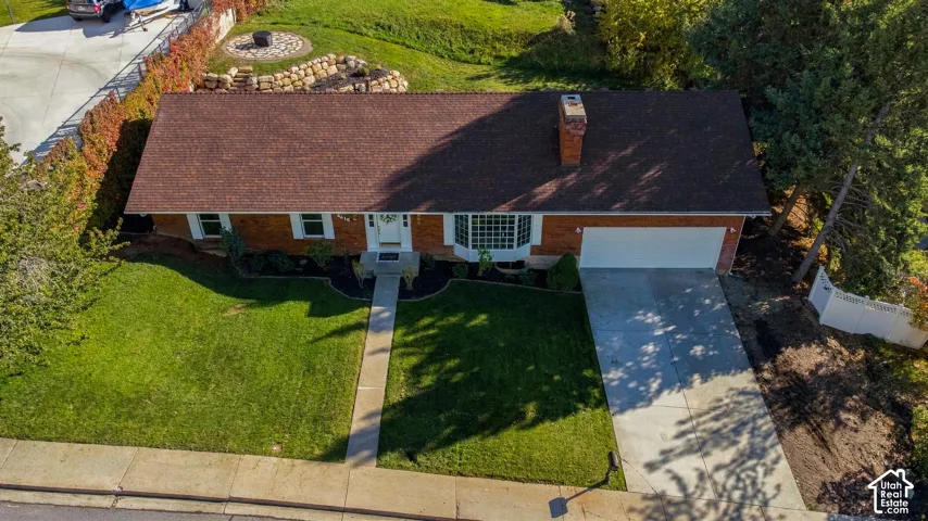 Single-story brick exterior featuring an asphalt shingle roof, bay window, masonry chimney, and concrete driveway