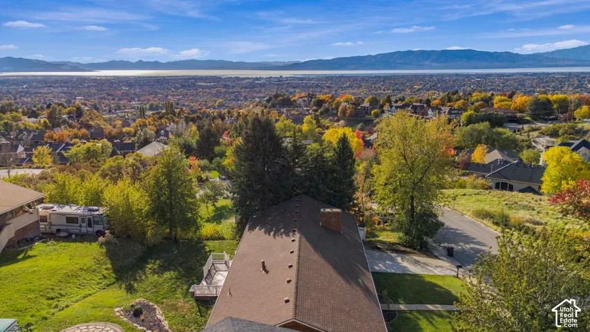Elevated lot with mature trees, a deck, a stone patio, and expansive scenery featuring distant mountains and a lake