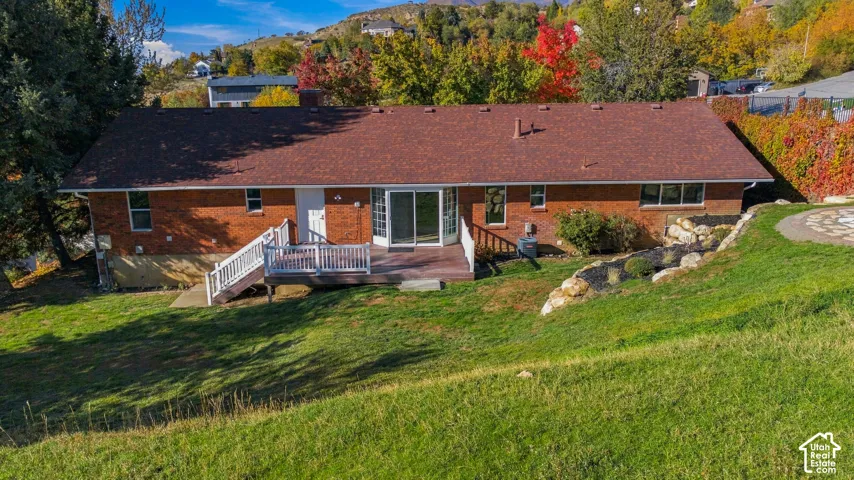 Brick exterior, asphalt shingle roof, tiered landscaping with stone accents, wood-finish deck with white railing, and sliding glass doors