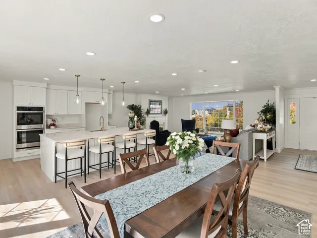 Open-concept living space featuring a central island with integrated seating, white cabinetry, built-in double wall ovens, recessed lighting, and wood-finish flooring