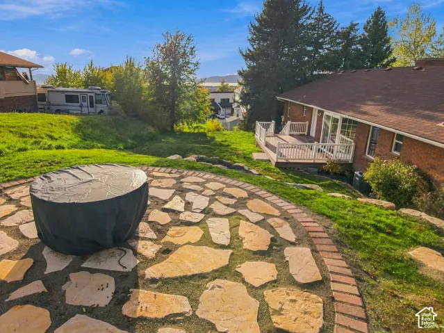Backyard featuring a flagstone patio with a brick border, elevated deck with white railing, and a sloped lawn