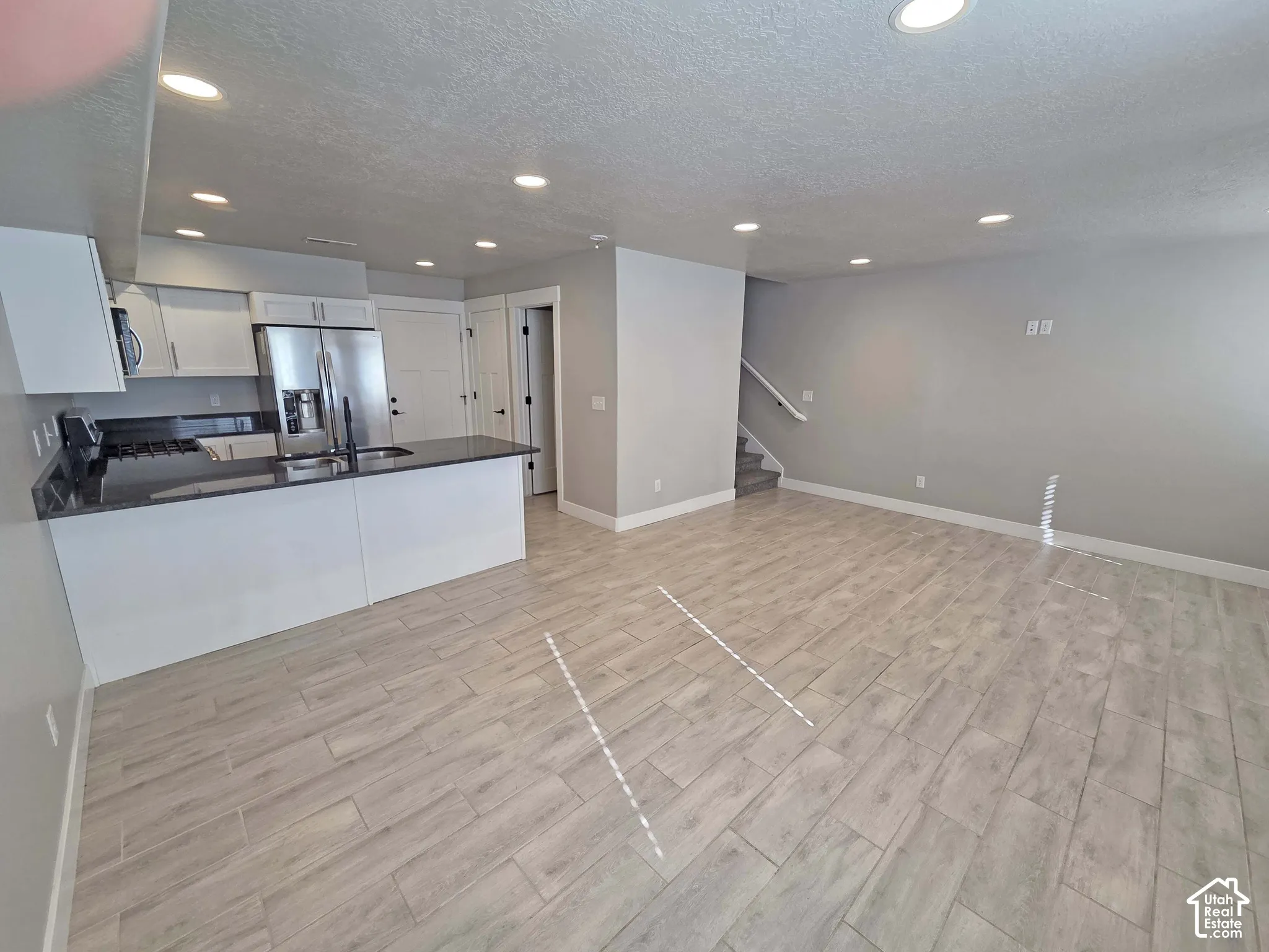 Open-concept kitchen featuring white cabinetry, dark countertops, a stainless steel refrigerator, recessed lighting, and wood-finish tile flooring