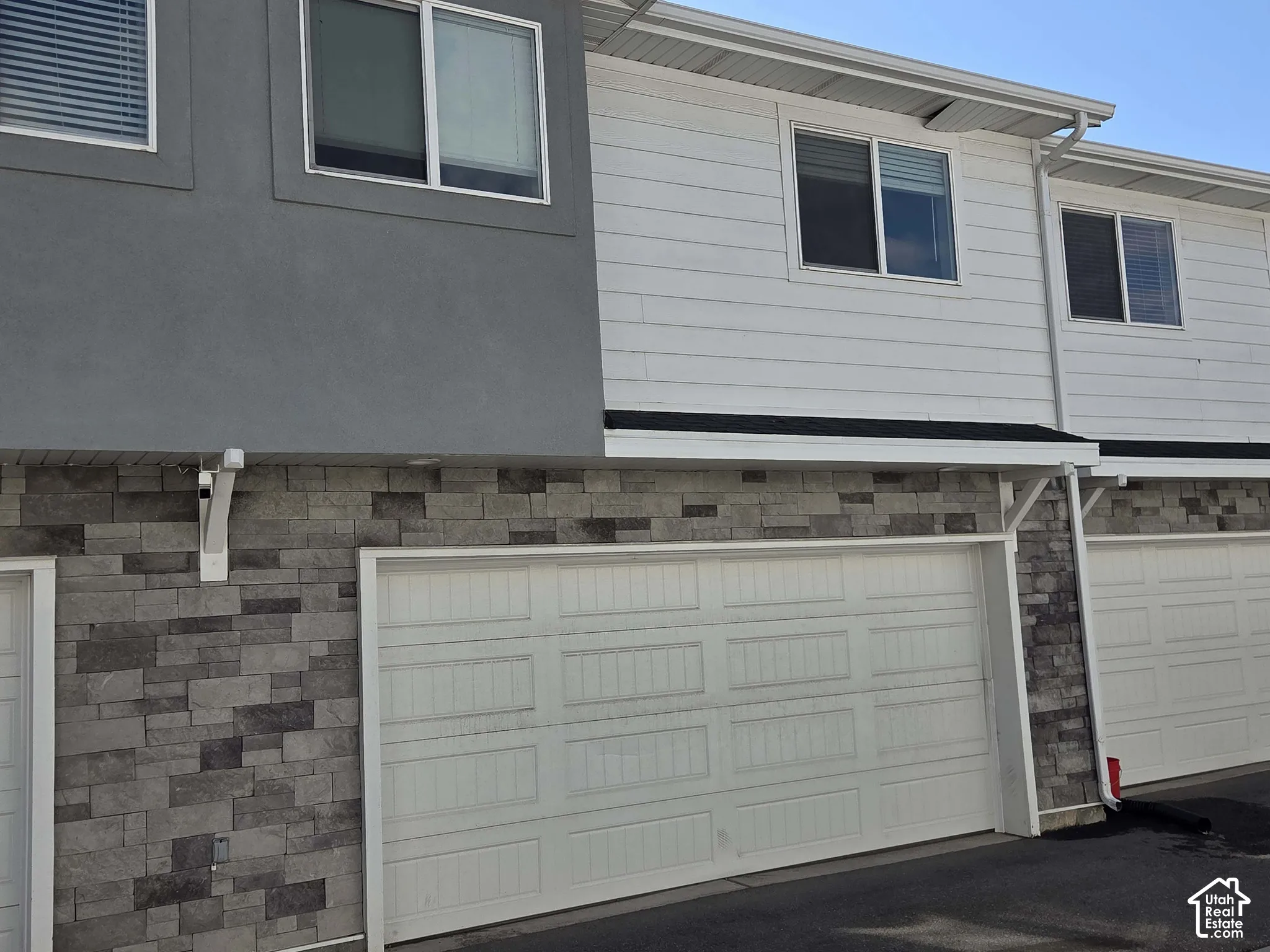 Multi-story exterior featuring a combination of horizontal siding, stucco-finish siding, and decorative stone veneer, complemented by a paneled garage door