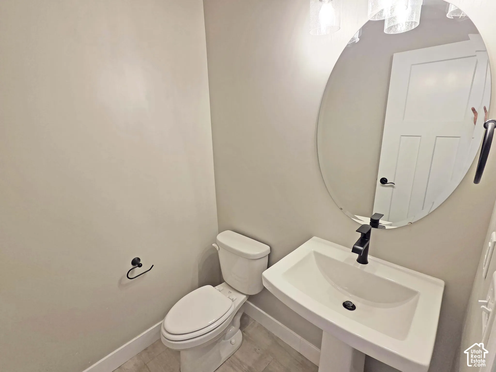 Powder room featuring a wall-mounted oval mirror, pedestal sink with matte black faucet, and hard-surface flooring