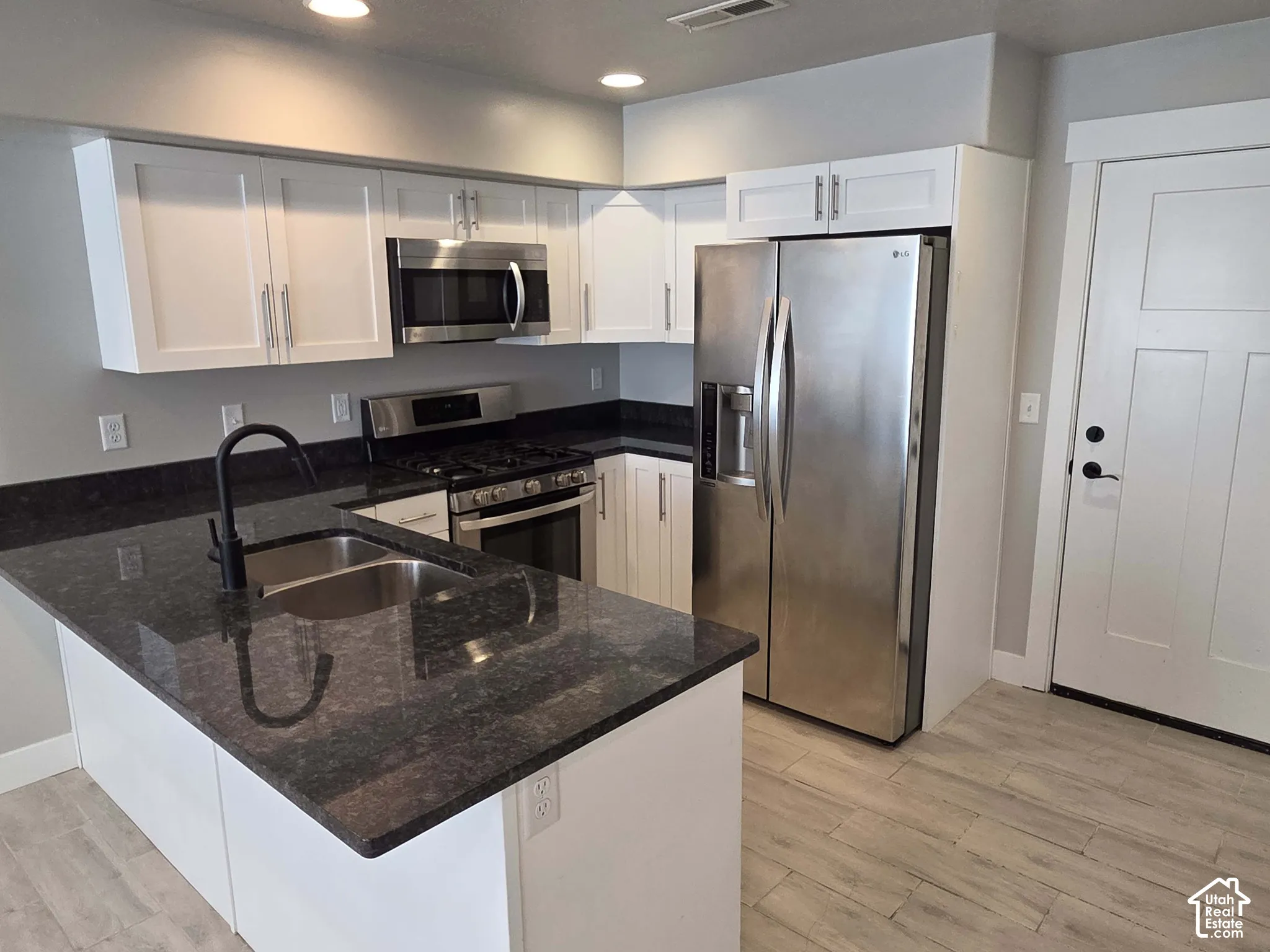 Kitchen featuring white cabinetry, dark stone countertops, stainless steel appliances, a double-basin sink with a matte black faucet, and wood-finish flooring