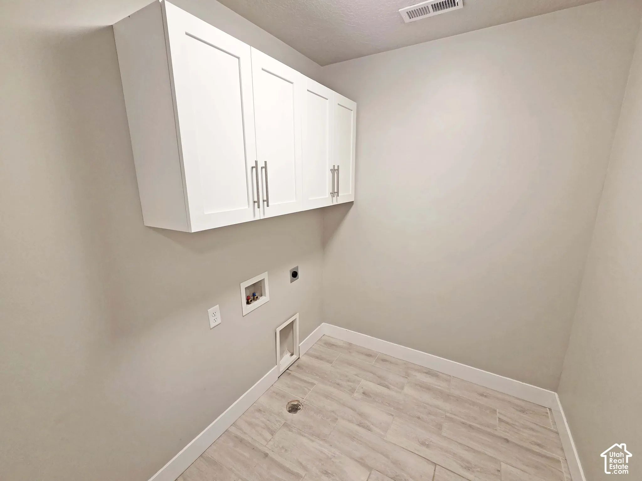 Utility area featuring wood-finish tile flooring and white shaker-style wall-mounted cabinetry with metallic bar pulls