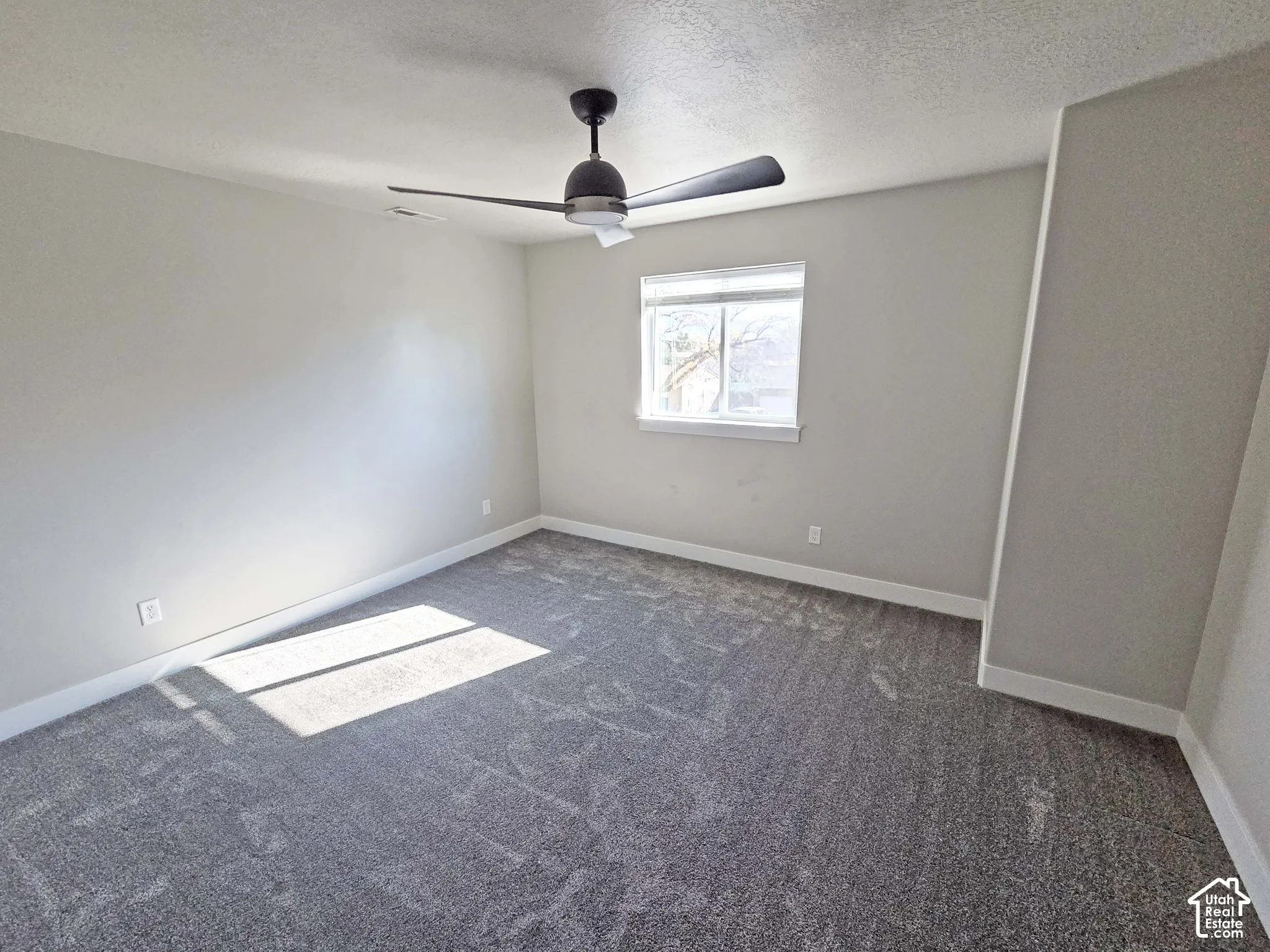 Neutral-toned walls, wall-to-wall carpeting, single-pane window, and a ceiling-mounted fan with integrated lighting