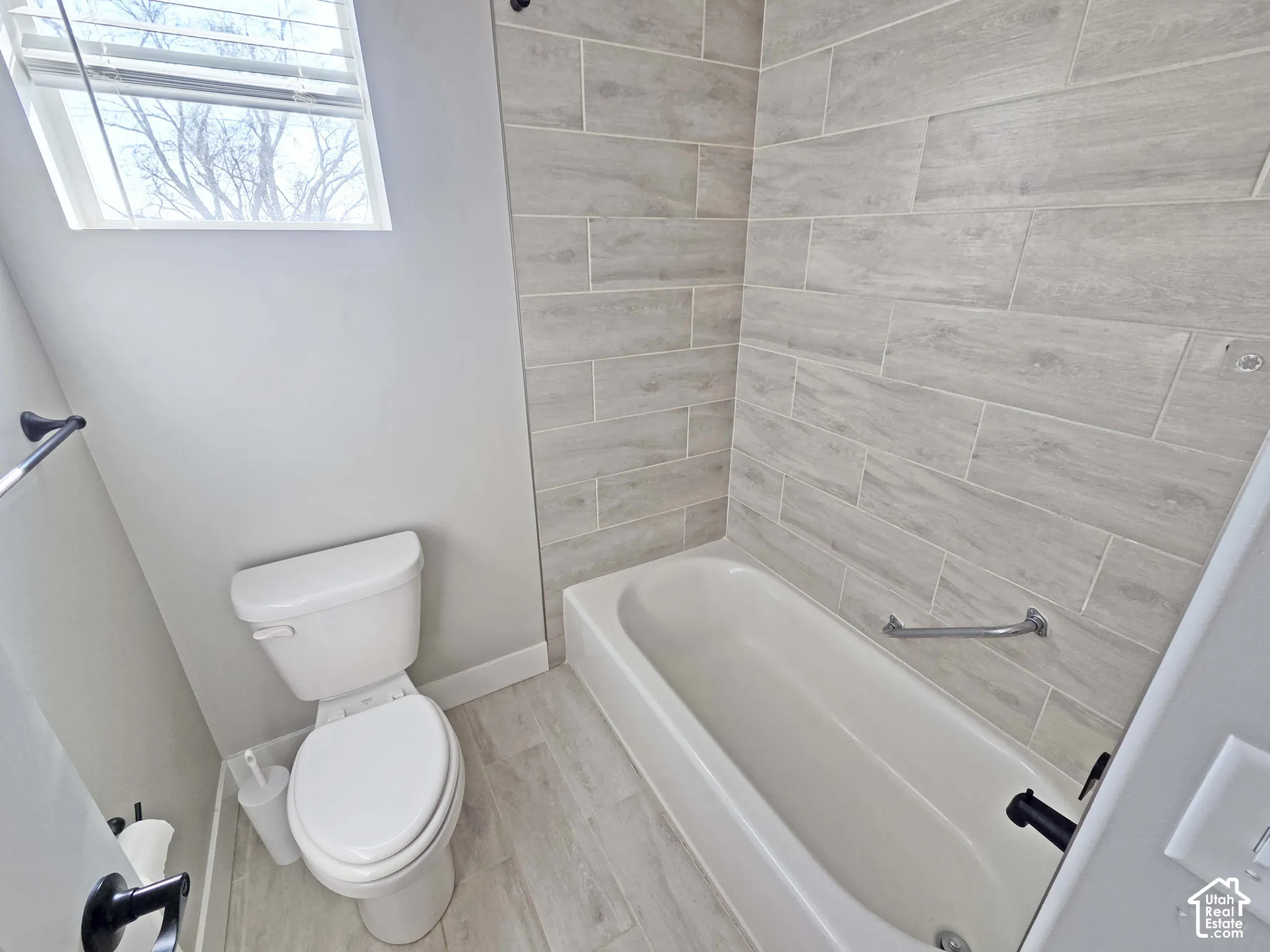 Bathroom featuring wood-finish tile surround in the tub area, tile flooring, and matte black plumbing fixtures