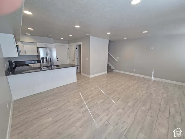 Open-concept kitchen featuring white cabinetry, dark countertops, a stainless steel refrigerator, recessed lighting, and wood-finish tile flooring