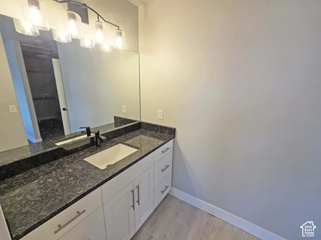 White vanity with shaker-style cabinetry, dark stone-finish countertop, undermount rectangular sink, matte black faucet, and five-light vanity fixture