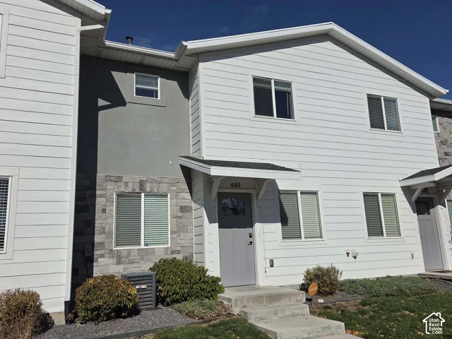 Exterior featuring white horizontal siding, stone veneer accents, gray entry door with glass pane, and dual-pitched roof gables