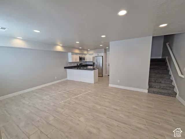 Open floor plan featuring wood-finish tile flooring, recessed lighting, white cabinetry, dark stone-style countertops, and stainless steel kitchen appliances