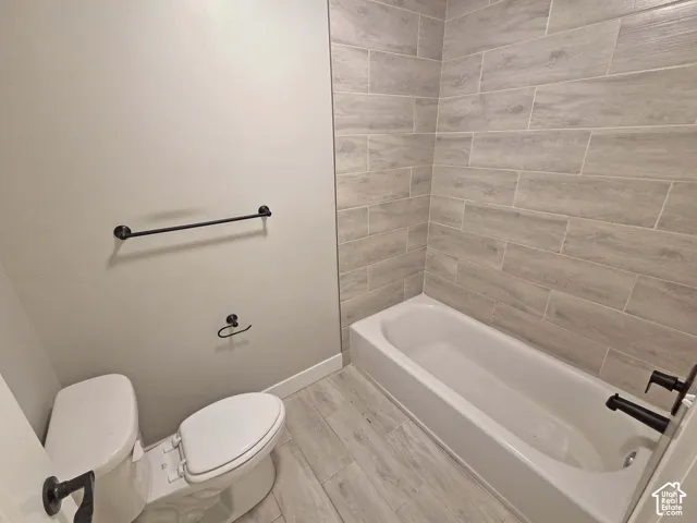 Bathroom featuring wood-finish tile flooring, a bathtub with full-height wood-finish tile surround, and matte black plumbing fixtures