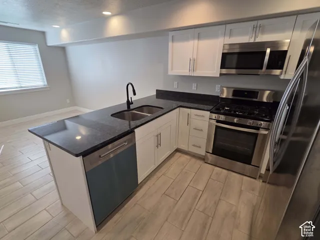 Kitchen featuring white cabinetry, dark stone countertops, stainless steel appliances, a dual-basin undermount sink with a matte black faucet, and wood-finish flooring