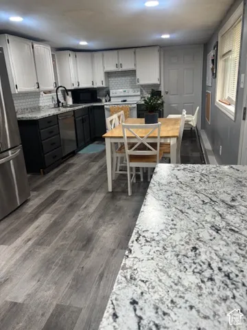 Kitchen featuring two-tone cabinetry, stone-finish countertops, subway tile backsplash, stainless steel appliances, and wood-finish flooring