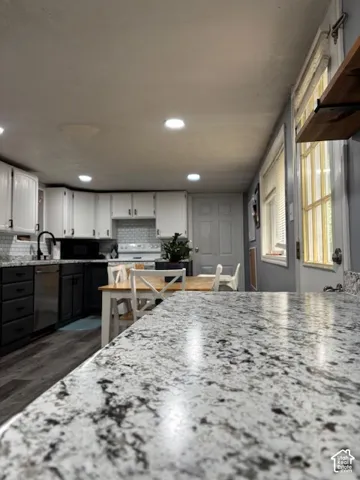 Kitchen featuring stone-finish countertops, two-tone cabinetry, subway tile backsplash, recessed lighting, and wood-finish flooring