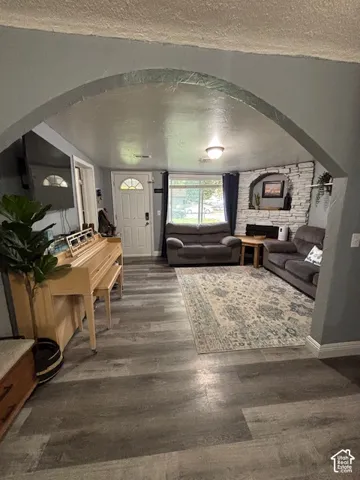Architectural arched entryway opening to a living area featuring wood-finish flooring, a white brick corner fireplace with a stone-texture mantel, and a multi-panel exterior door with a decorative glass insert