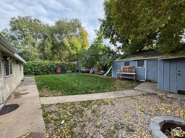 Backyard featuring a manicured lawn, concrete patio area, detached storage structure, and stone-bordered fire pit