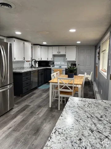 Kitchen featuring two-tone cabinetry, stone-finish countertops, subway tile backsplash, stainless steel appliances, and wood-finish flooring