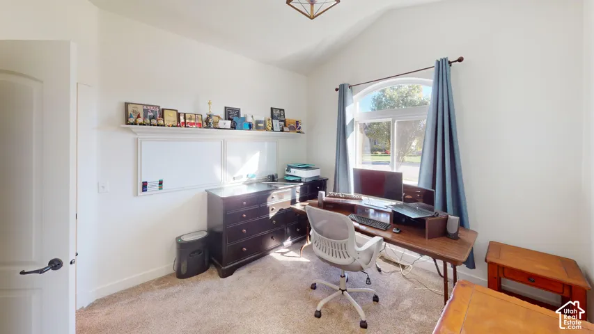 Vaulted ceiling, arched window, wall-mounted display shelf, and neutral carpeting