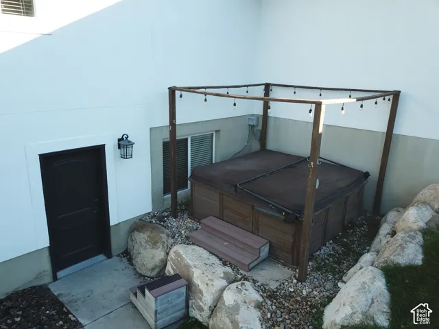 Exterior patio area featuring a built-in spa, dark-toned wooden pergola, natural stone landscape accents, and an attached wall-mounted lantern