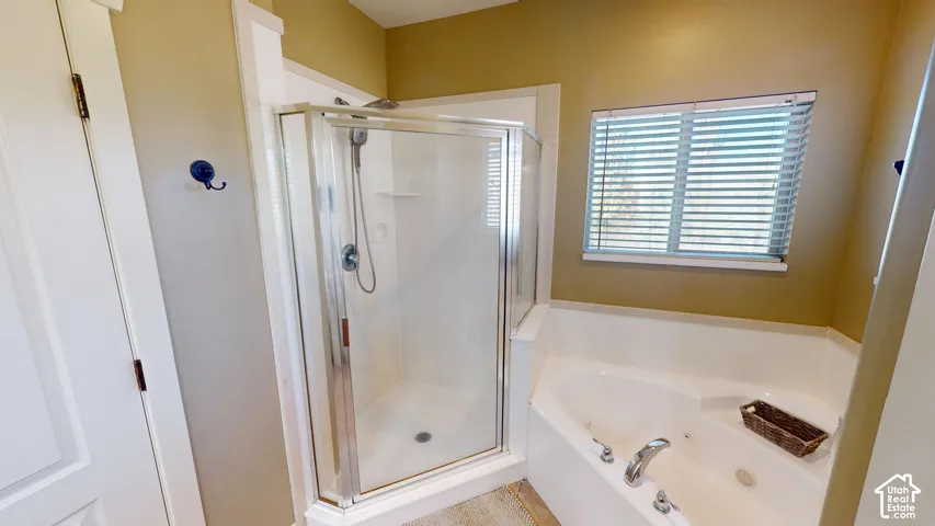 Corner jetted soaking tub and separate glass-enclosed shower stall with a hand-held sprayer, finished with white fixtures and horizontal blinds