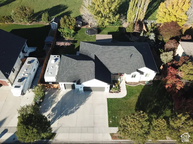 Single-level residence featuring a multi-car garage, concrete driveway, and expansive rear lawn with mature landscaping