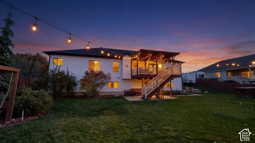 Multi-level exterior featuring a covered deck with white railing, wood-frame staircase, concrete patio, and string lighting