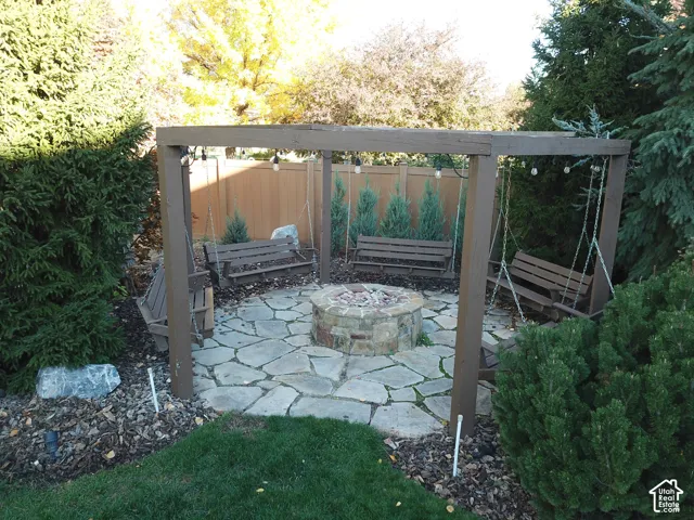 Stone fire pit set within a flagstone patio, framed by a timber pergola and enclosed by privacy fencing
