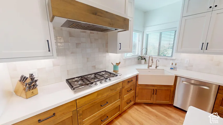 Kitchen featuring white cabinetry paired with wood-finish base cabinets, a white apron-front sink, a stainless steel gas cooktop, and a matching wood-finish range hood
