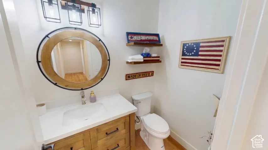 Bathroom featuring a vanity with a light-finish wood cabinet and a stone-composite countertop, a circular wood-framed wall mirror, a three-light fixture with black metal cage shades, and floating wood-finish wall shelves