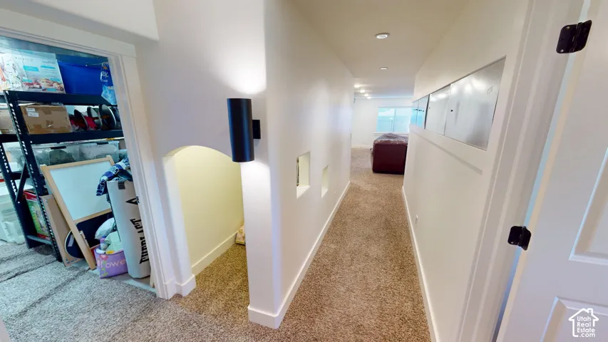 Hallway featuring carpeted flooring, recessed lighting, architectural wall niches, a cylindrical wall-mounted light fixture, and horizontal inset panels