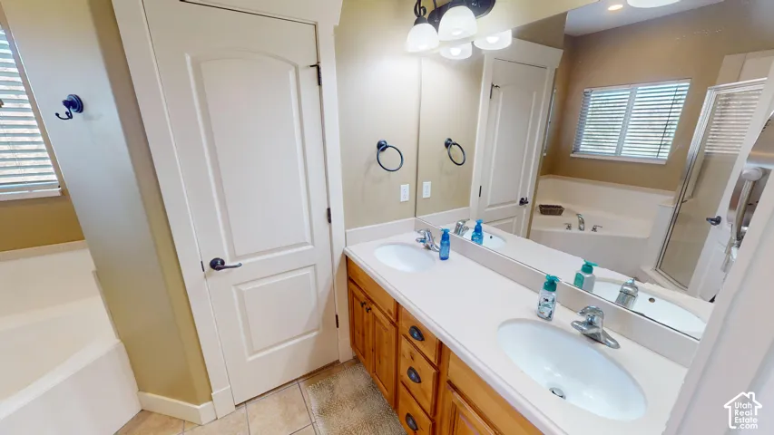 Dual-sink vanity with light-tone solid surface countertop, wood cabinetry, built-in soaking tub, and enclosed glass shower