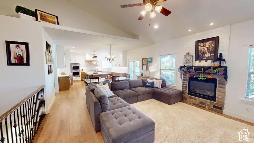 Vaulted ceilings with recessed lighting, stone-surround fireplace with horizontal shiplap detailing, wood-finish flooring, and wrought-iron staircase railing