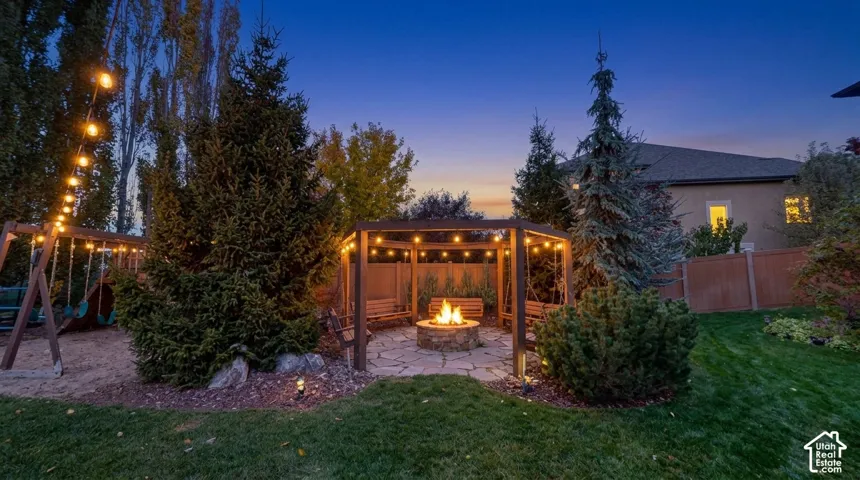 Expansive backyard featuring a stone-paver patio, circular stone fire pit, wood-frame gazebo, and mature evergreen trees