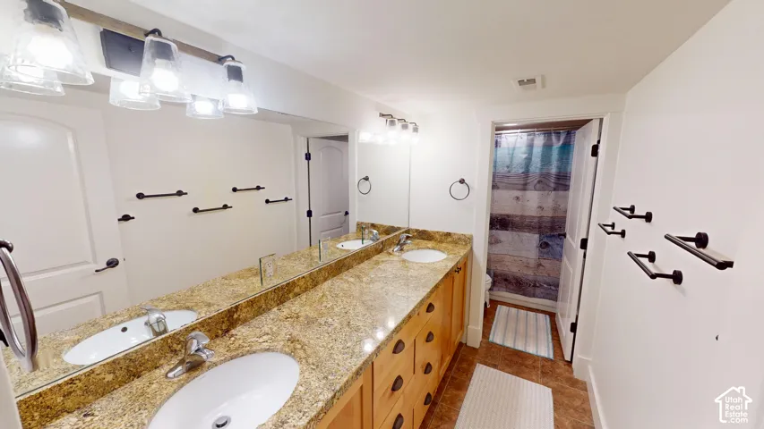 Double vanity featuring stone-finish countertops, undermount sinks, custom wood cabinetry, and matte black hardware