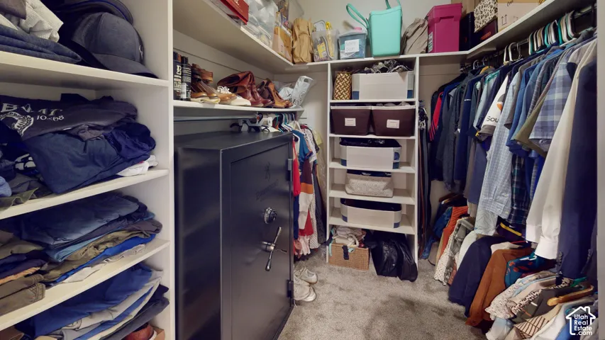 Walk-in closet featuring floor-to-ceiling white built-in shelving, multiple hanging rods, and a heavy-duty bolt-down floor safe